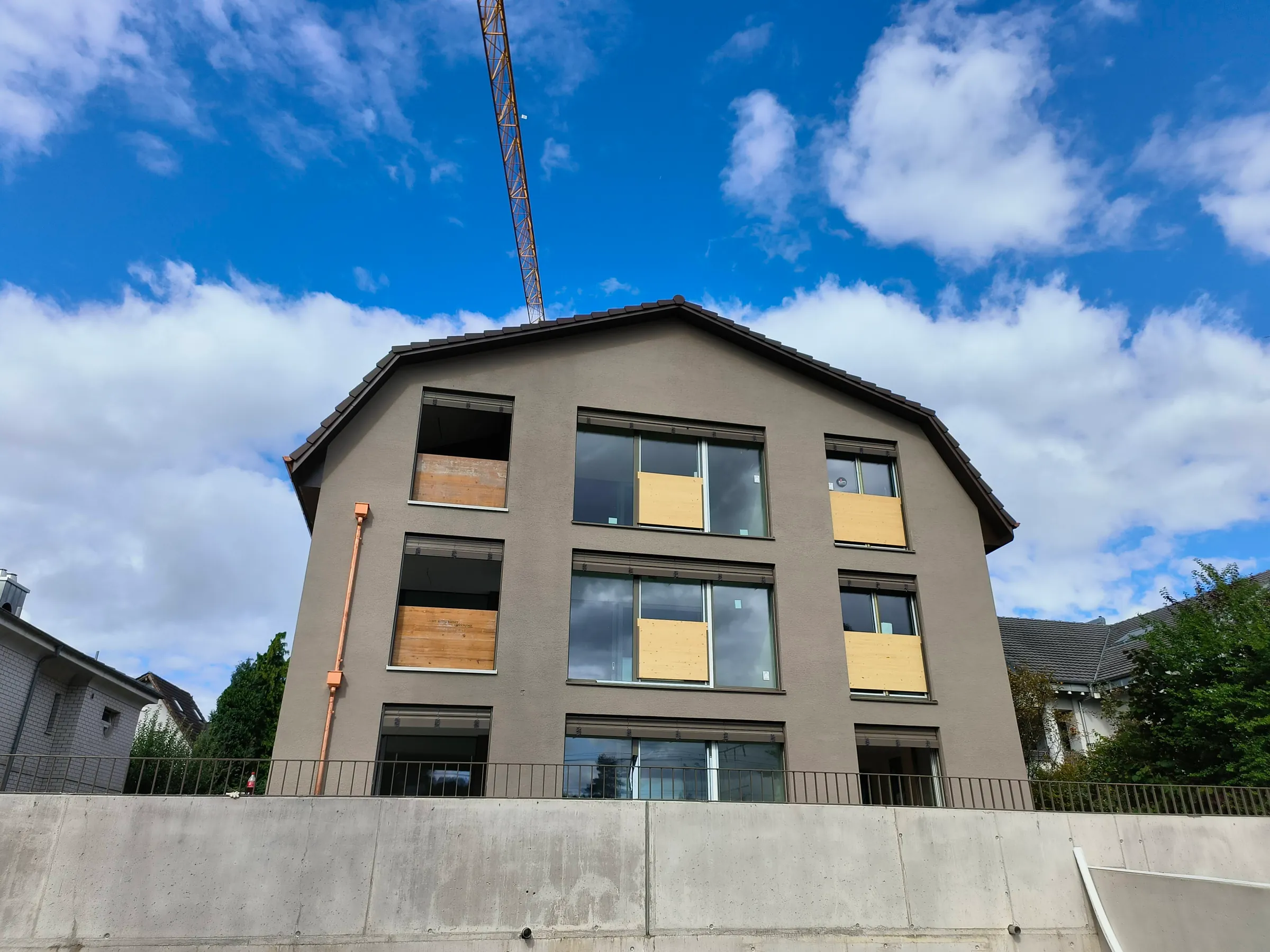 Dreigeschossiges Mehrfamilienhaus mit neuem Satteldach im Bau in Therwil, Baukran und blauer Himmel
