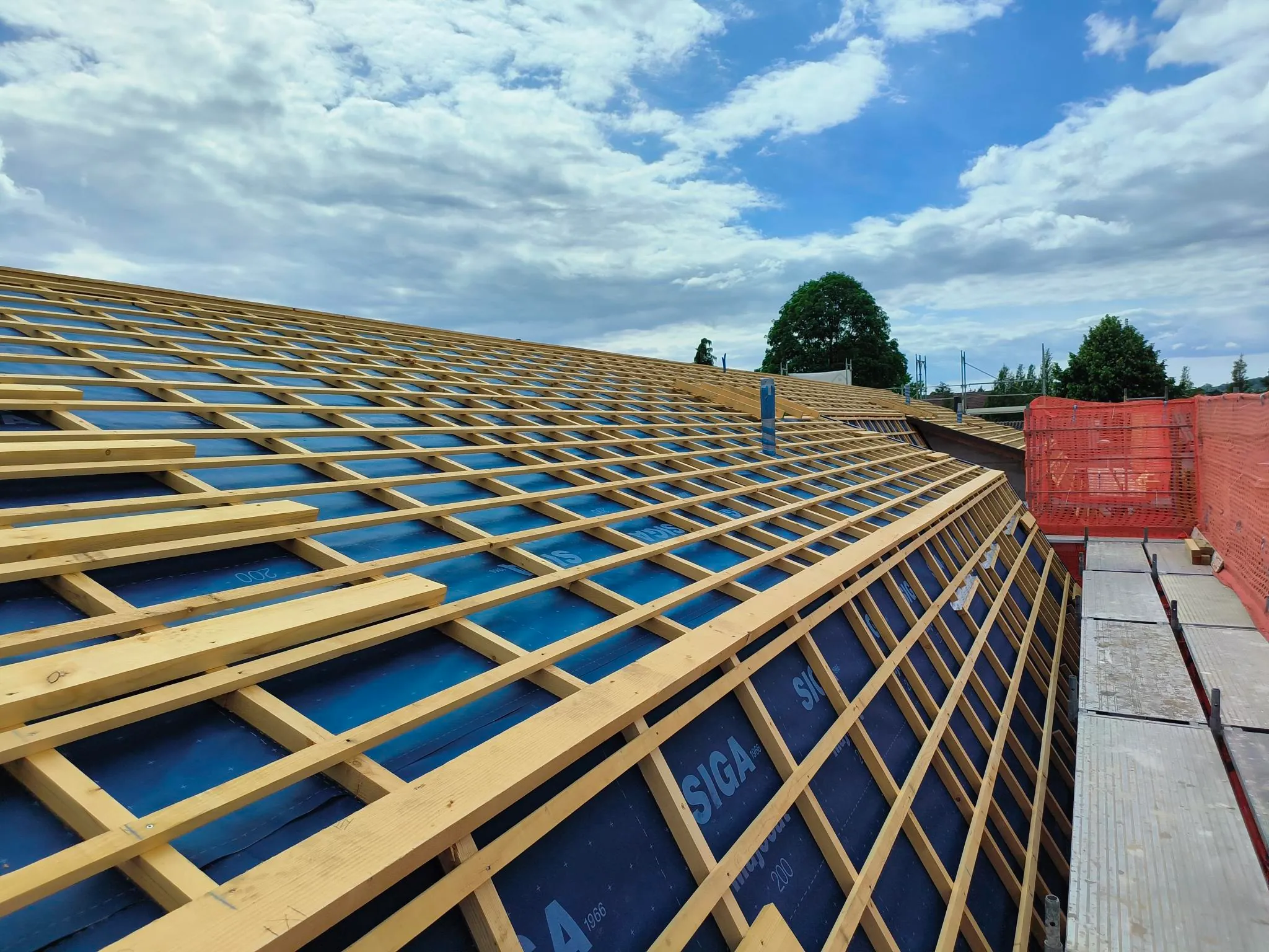 Blaue Unterdachbahn mit Konter- und Dachlattung auf dem Neubau in Therwil, Gerüst mit roten Netzen