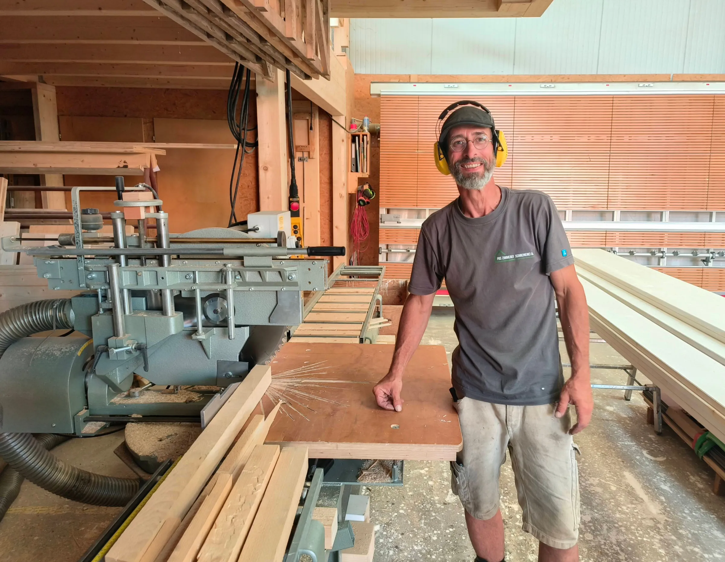 Marco Cavigelli, Zimmermann Vorarbeiter, mit Gehörschutz an einer Holzbearbeitungsmaschine in der Werkstatt