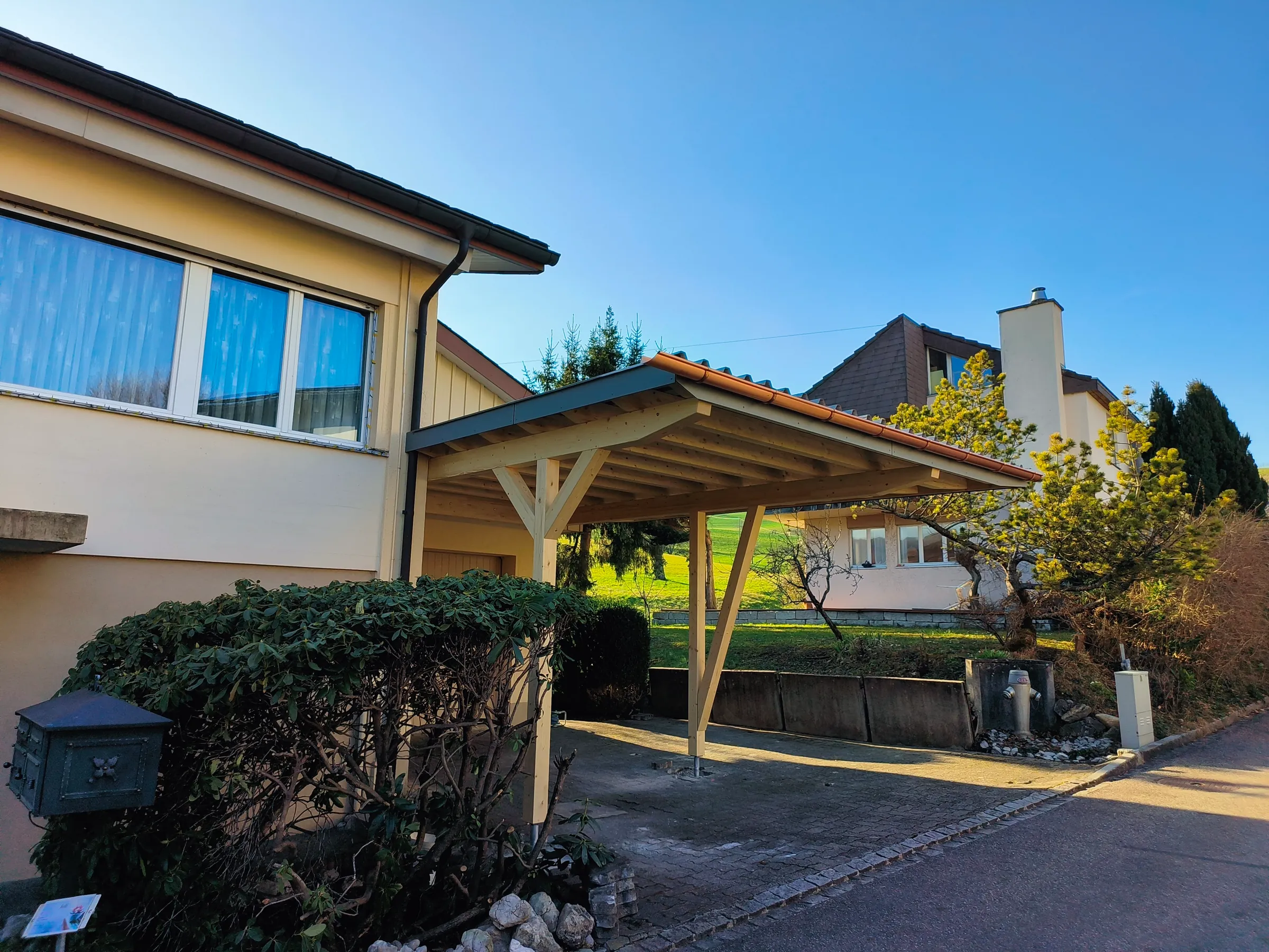 Holz-Carport in Niederdorf von der Seite, daneben Wohnhaus und Garten