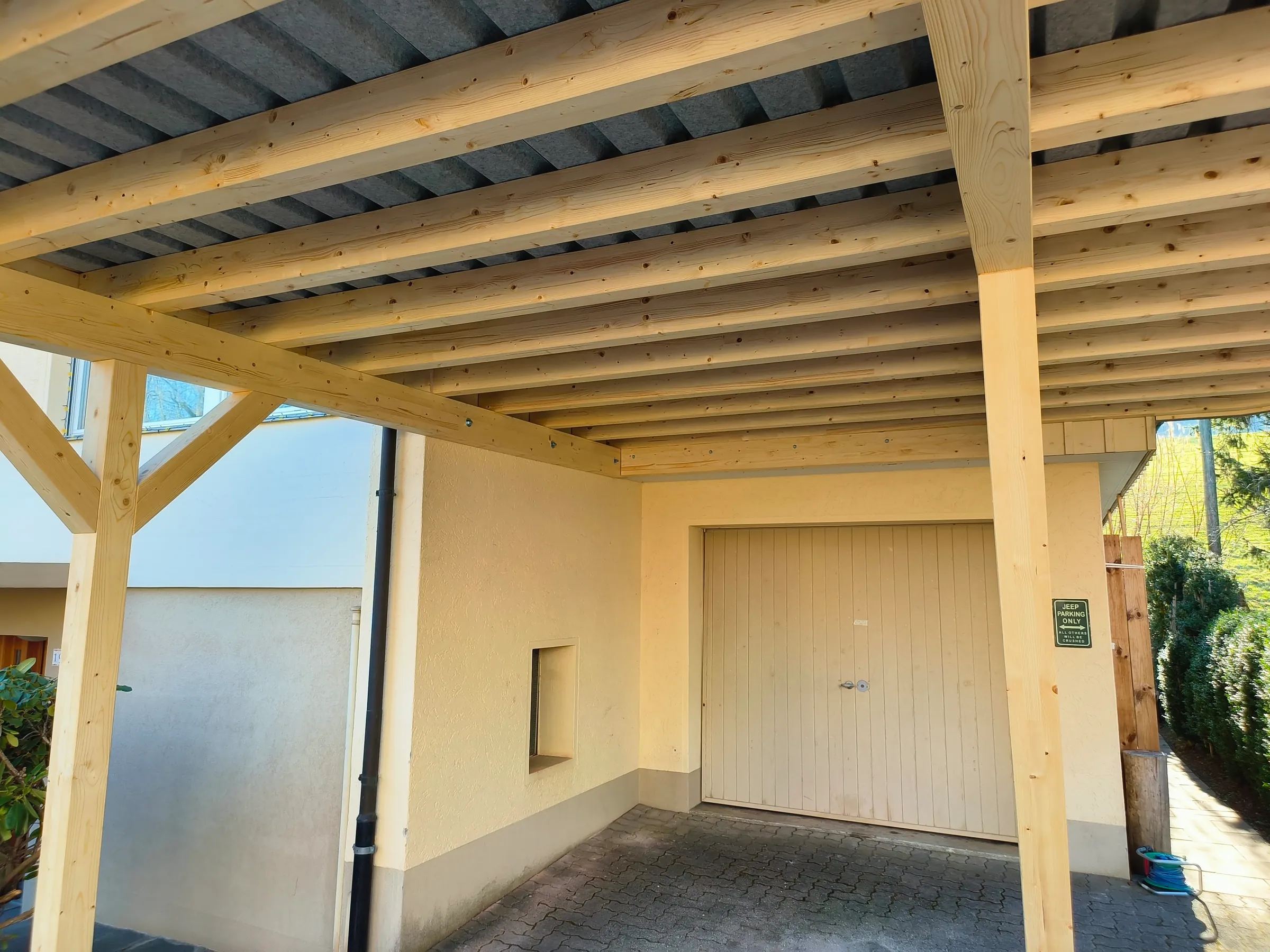 Untersicht einer Carport-Holzkonstruktion mit Wellblech unter der Eindeckung, dahinter ein Garagentor