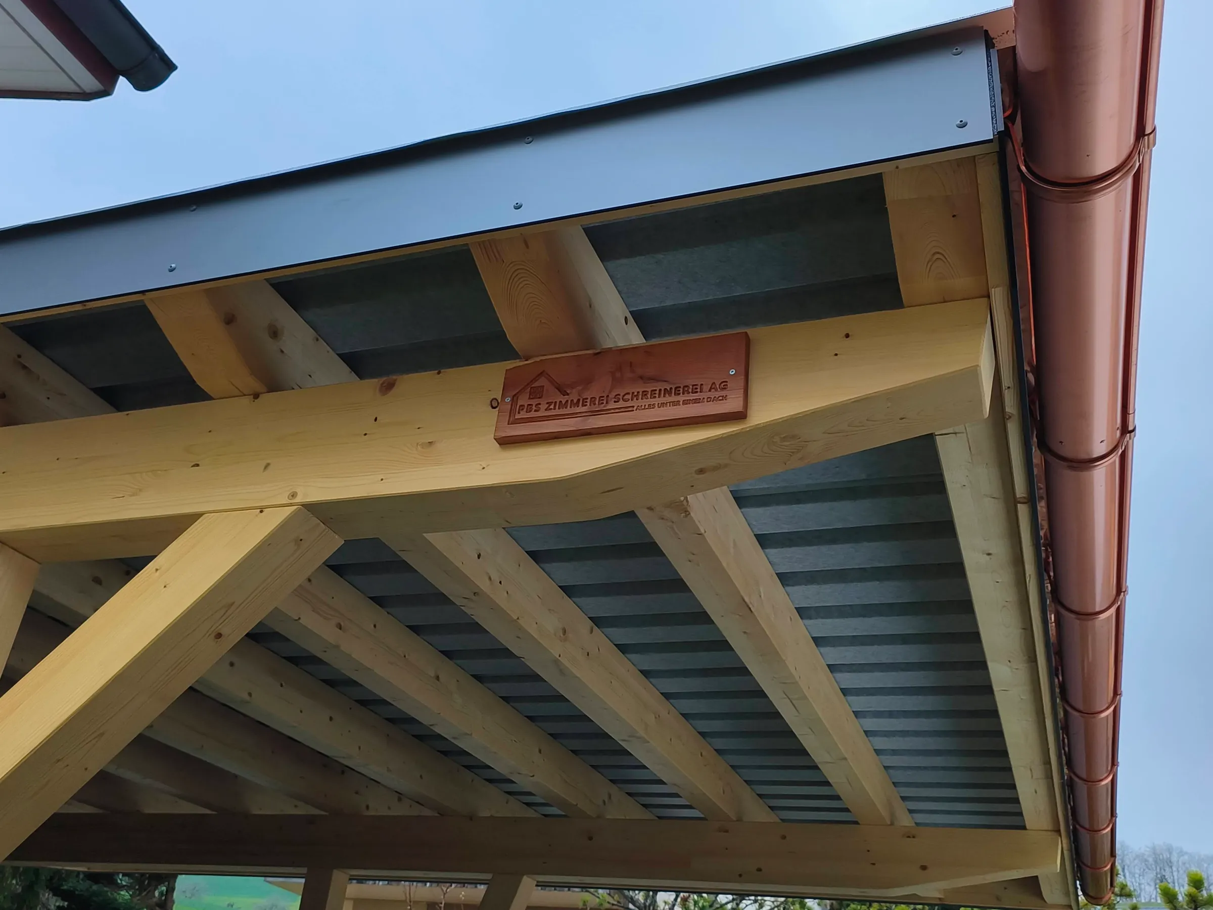 Firmenschild an der Pfette eines Holzdachs, daneben die Kupfer-Dachrinne