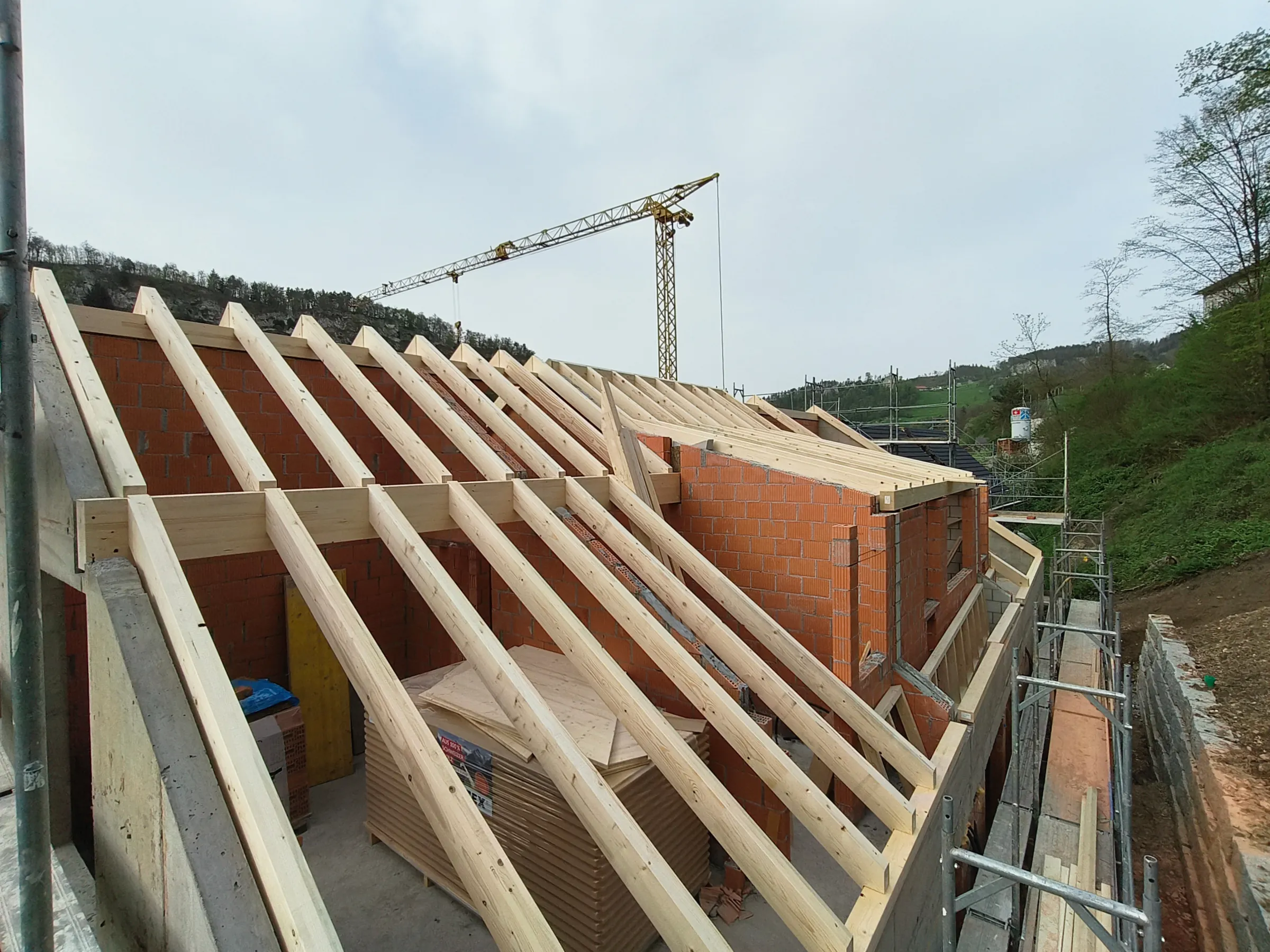 Sparrenlage eines neuen Dachstuhls auf Mauerwerk in Duggingen, Baukran im Hintergrund