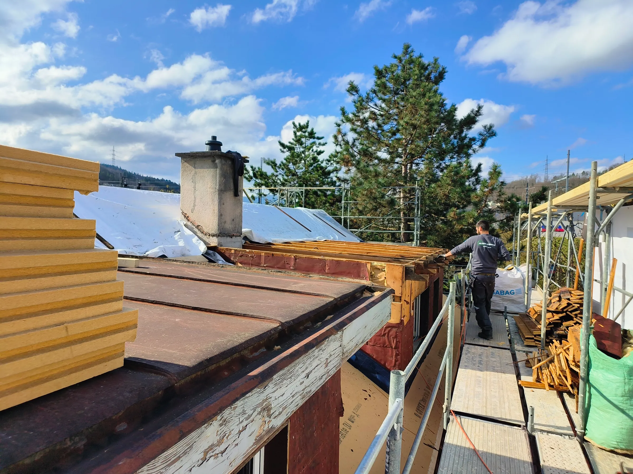 Rückbau am Dachrand in Liestal: Arbeiter auf dem Gerüst, Stapel Holzfaser-Dämmplatten und Schutzfolie