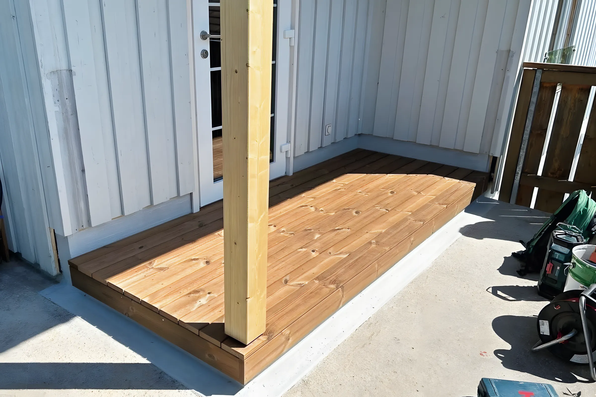 Neuer Holzrost auf einer Betonplatte neben einer Holzstütze beim Hauseingang
