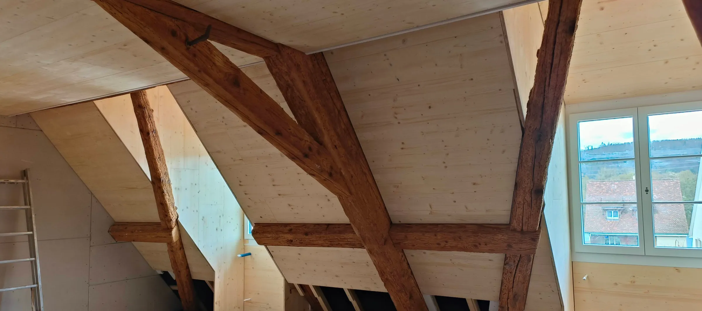 Ausgebautes Dachgeschoss mit dunklem altem Fachwerk vor hellen Verkleidungen aus Fichtenholz