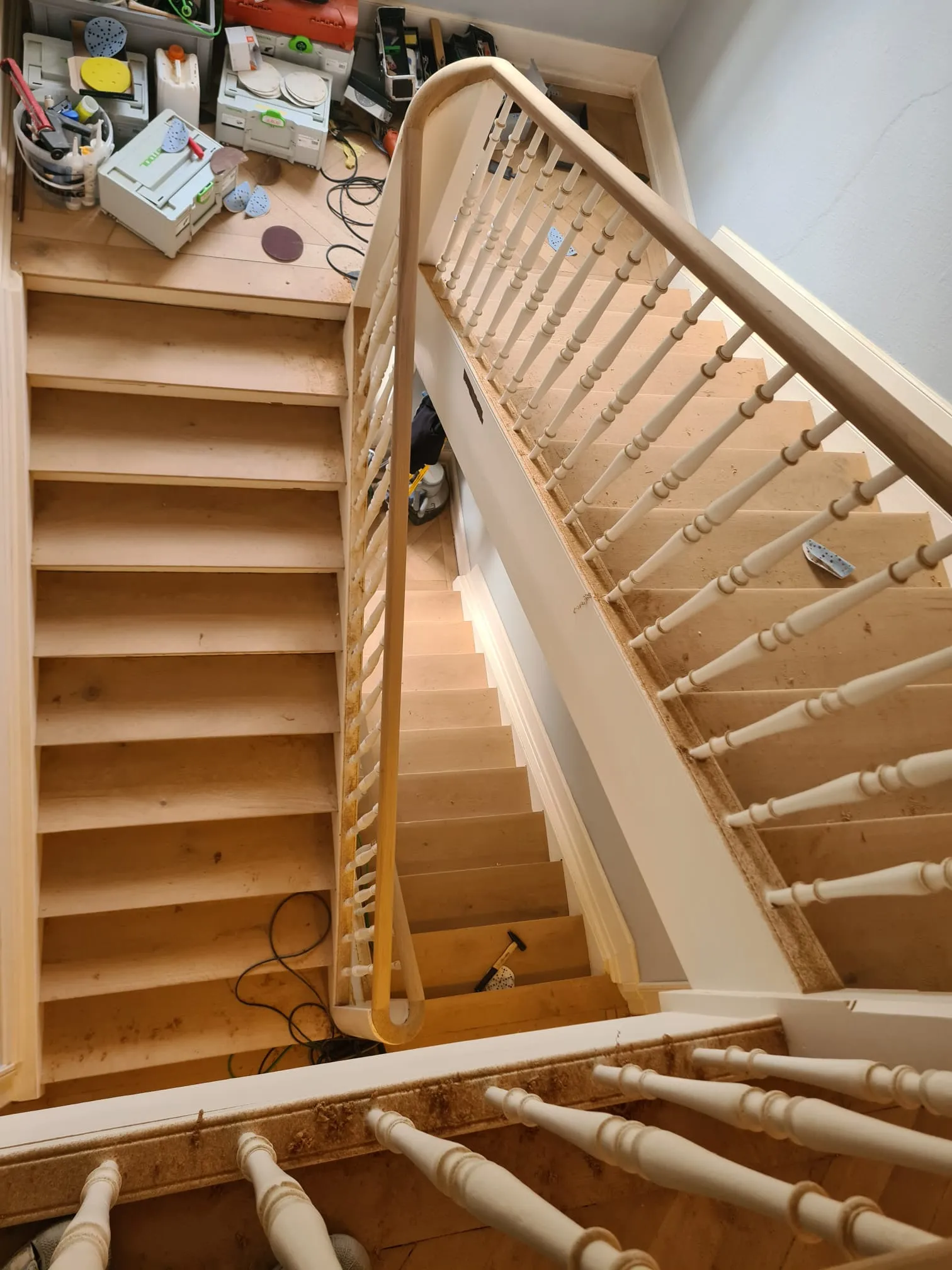Holztreppe mit gedrechselten Geländerstäben von oben, die Stufen roh geschliffen, oben stehen die Maschinen