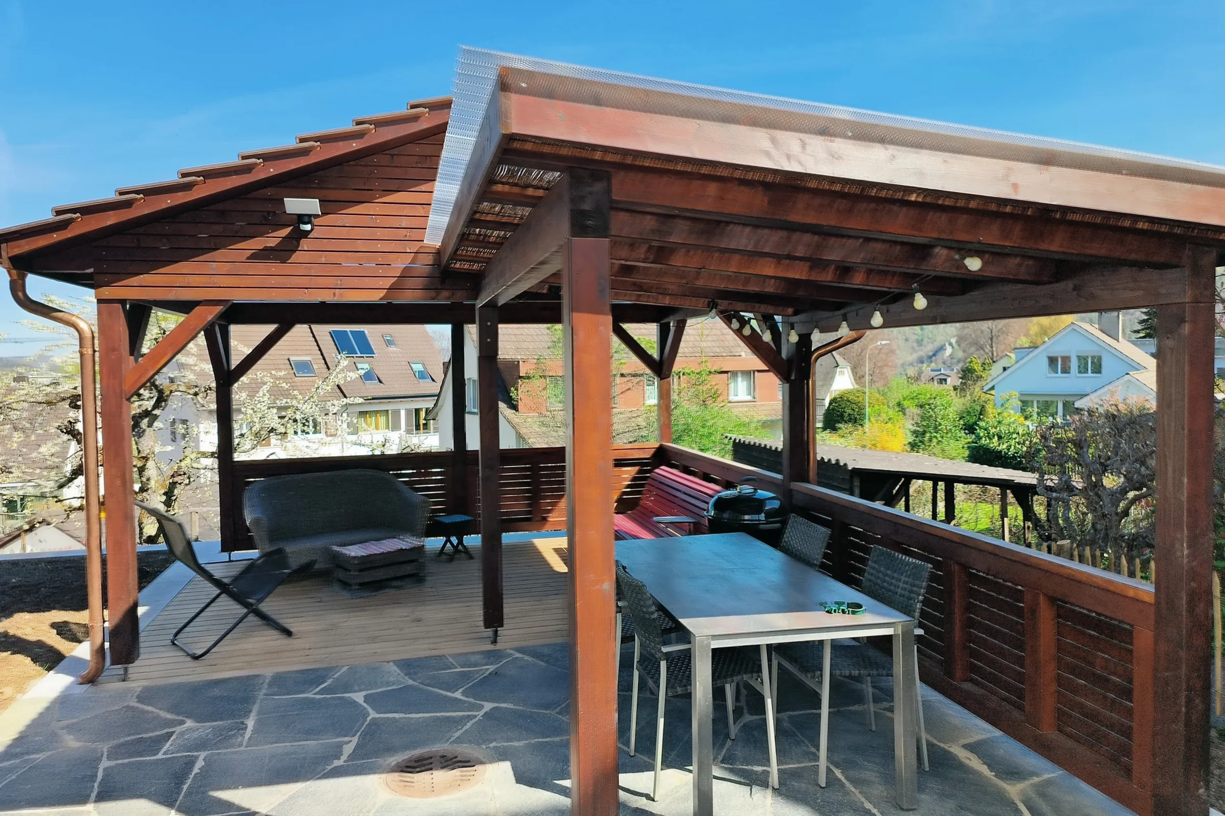 Gedeckter Sitzplatz aus braun lasierter Fichte mit Steil- und Flachdachteil, Gartentisch und Weitblick