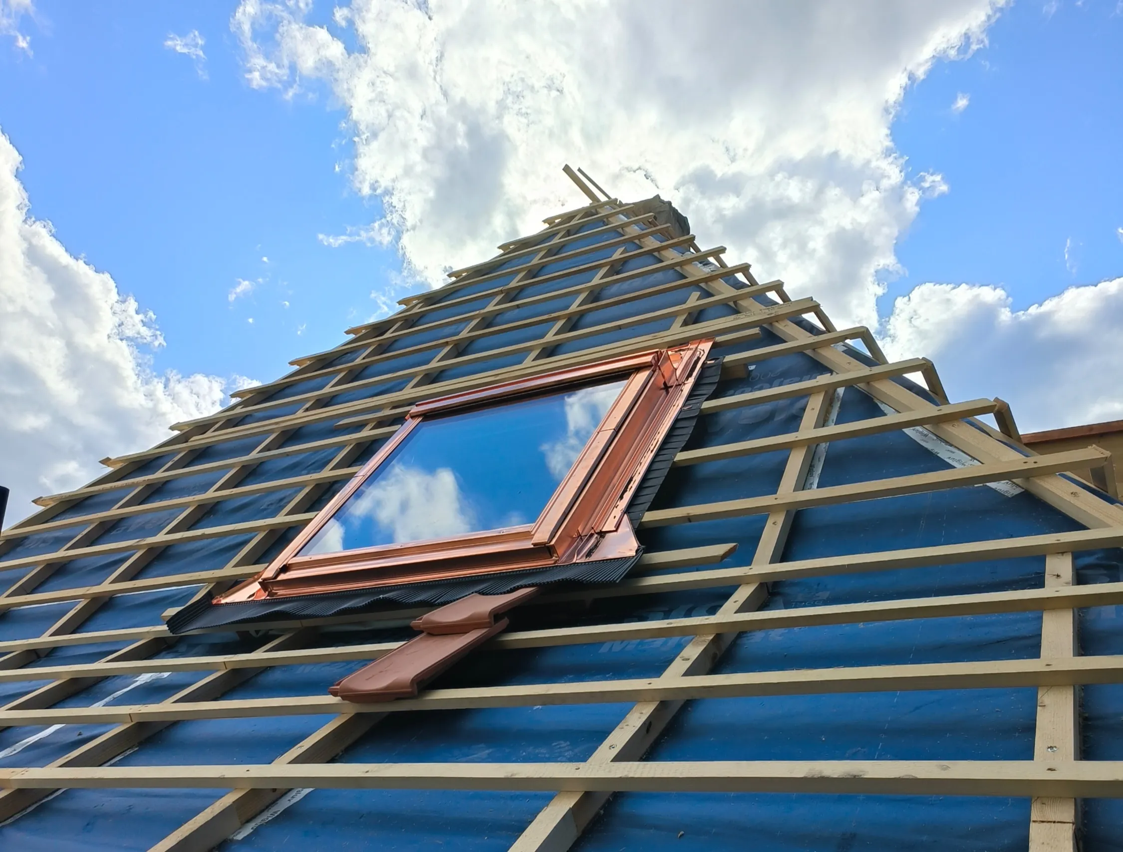 Velux-Dachfenster im Einbau auf der Lattung über blauer Unterdachbahn, von unten gegen den Himmel