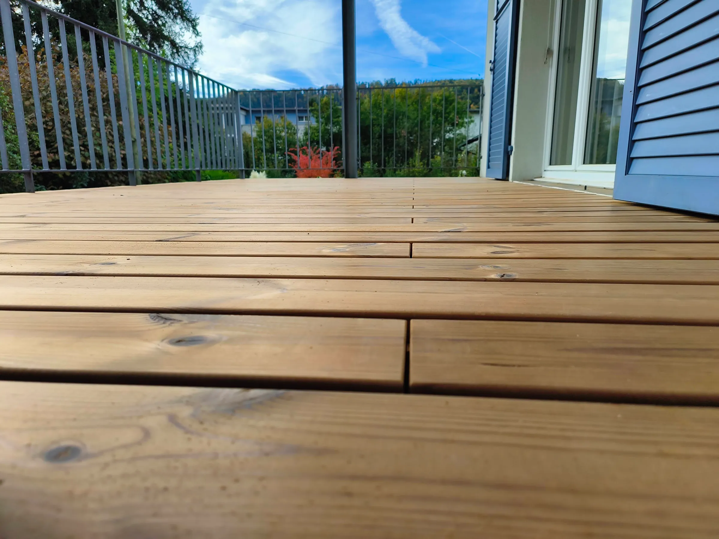Bodennahe Nahaufnahme der neuen Thermokiefer-Dielen auf dem Balkon, Geländer und Himmel