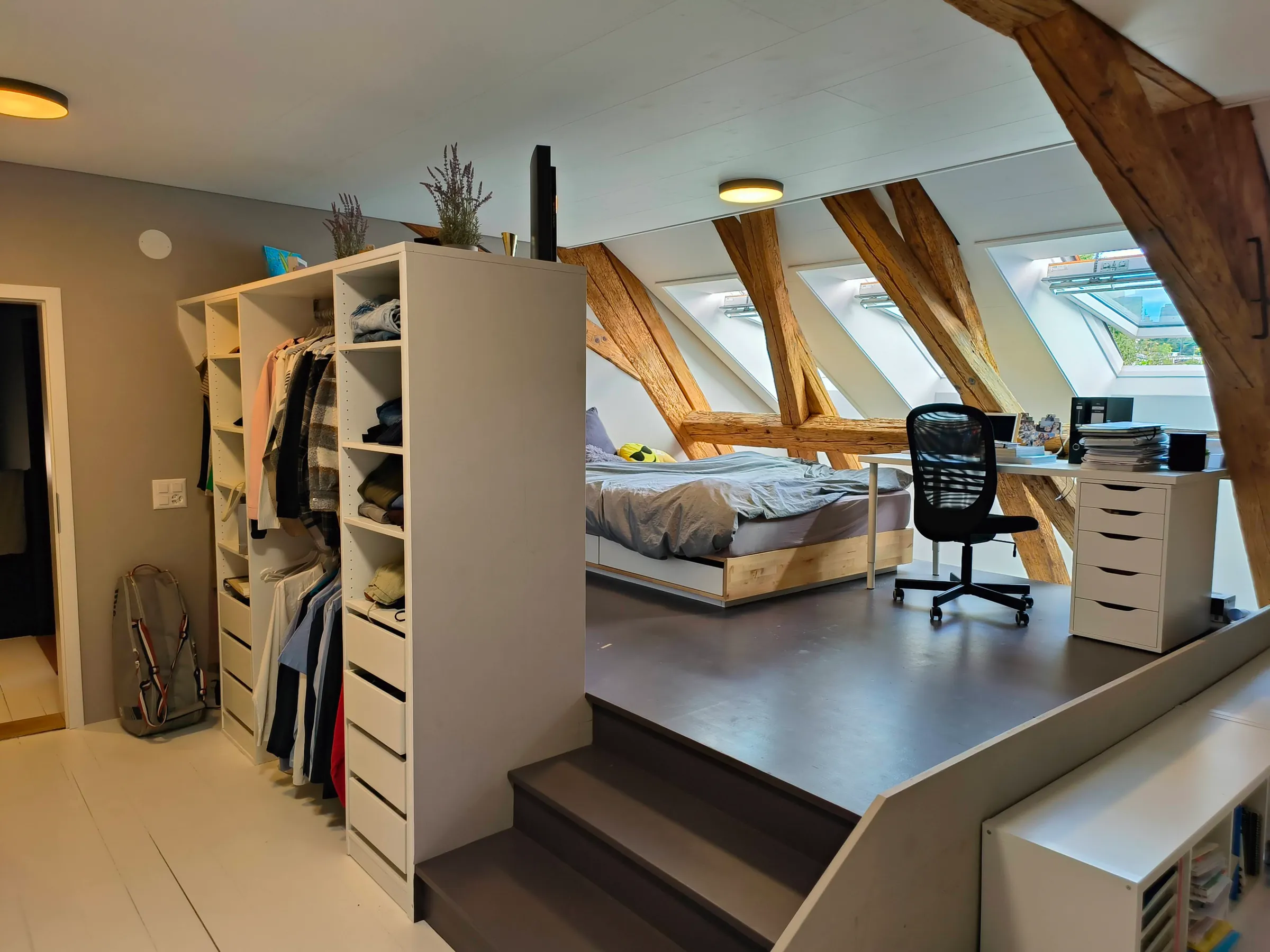 Schlafzimmer auf einem Podest unter drei neuen Dachfenstern, die alten Holzbalken bleiben sichtbar