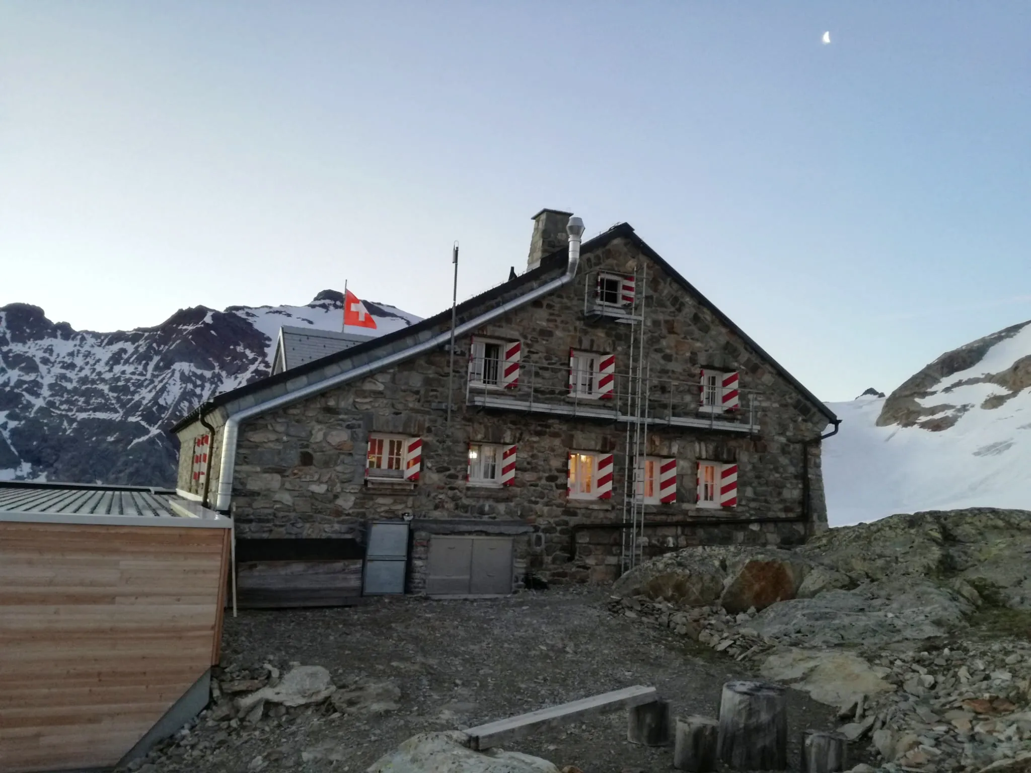 SAC-Hütte Tierbergli im Schnee: Steinbau mit rot-weissen Fensterläden, Schweizer Fahne und Holzanbau