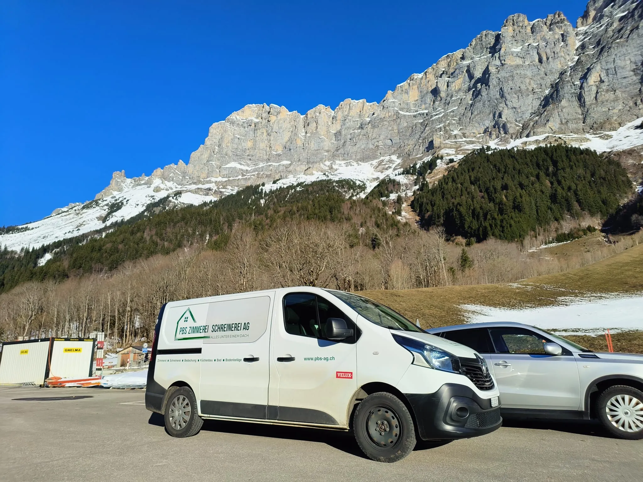 Beschrifteter Firmentransporter auf dem Parkplatz im Tal, darüber Kalkfelsen und Schnee