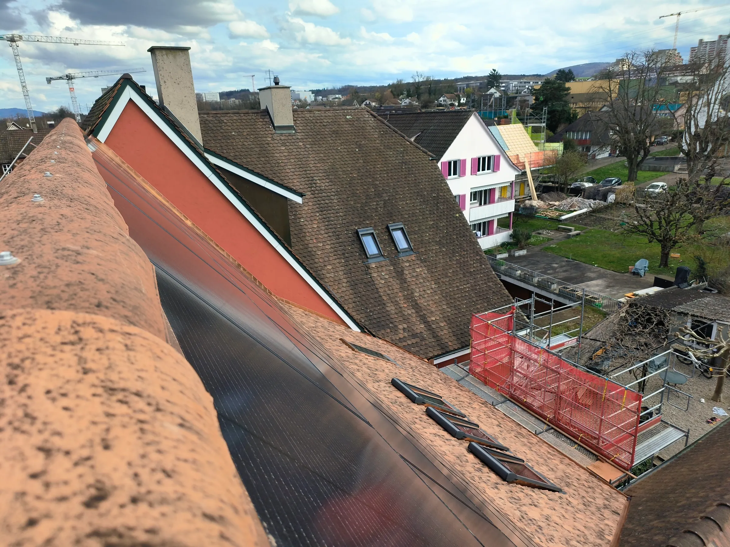Blick vom First über Ziegeldach mit Solarmodulen und Dachfenstern auf das Quartier in Kaiseraugst